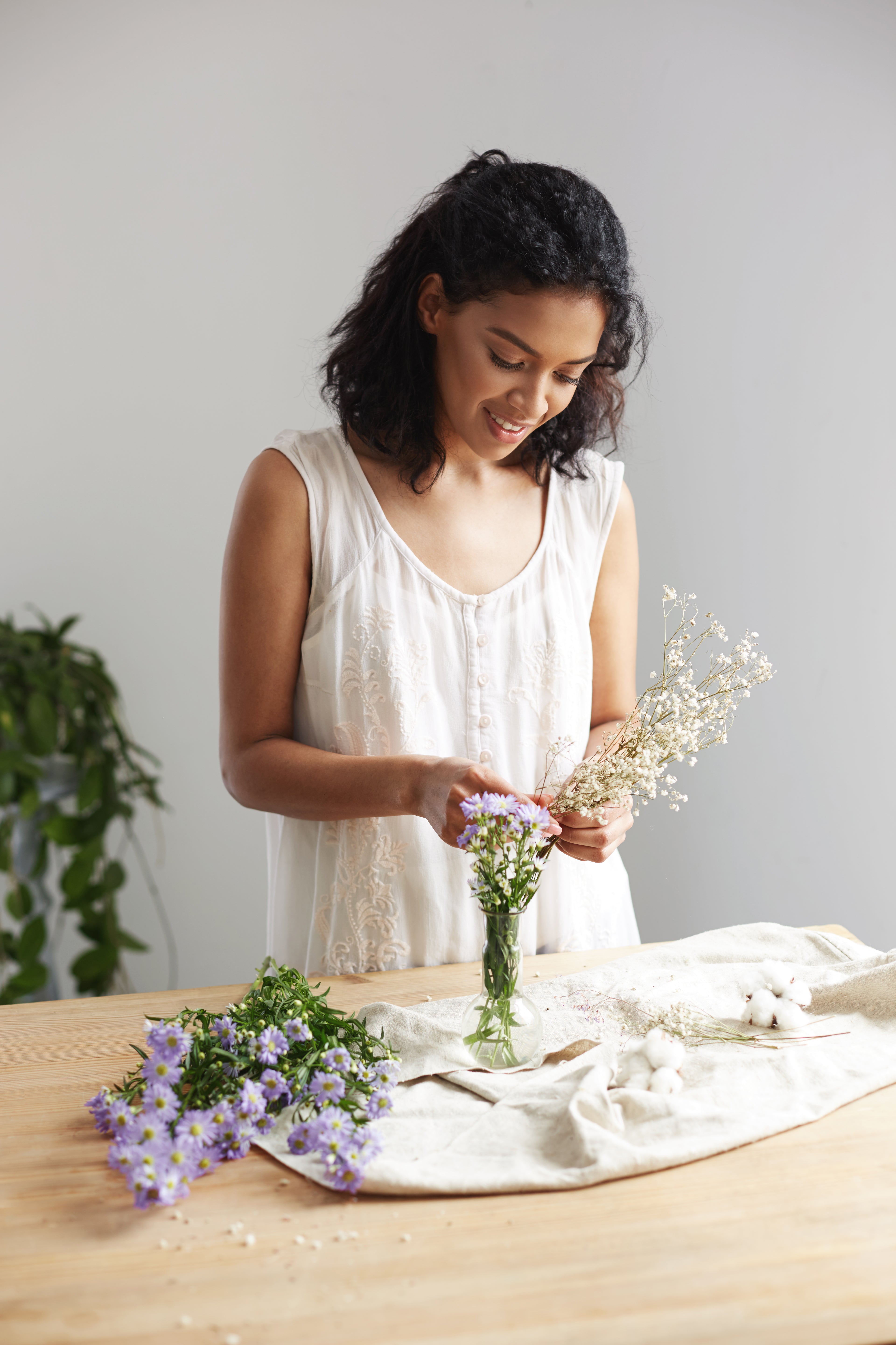 young-african-female-florist-smiling-working-with-bunch-flowers-workplace-white-wall.jpg